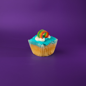 A vanilla cupcake with a Skittles candy filling, topped with blue vanilla buttercream, and finished with vanilla buttercream clouds and a rainbow candy piece. End of the Rainbow cupcake