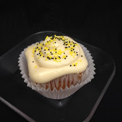 A lemon cupcake topped with honey cream cheese icing and finished with yellow and black nonpareils. Honey Lemon cupcake