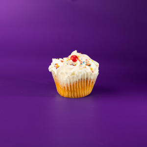 A vanilla cupcake filled with Skittles candy, topped with vanilla buttercream and rainbow nonpareils, and finished with a Skittles candy piece. Skittles cupcake