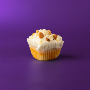 A white chocolate cupcake with chopped macadamia nuts baked in, topped with a vanilla buttercream and finished with white morsels and finely chopped macadamia nuts. White Chocolate Macadamia Nut cupcake