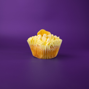 A banana cupcake with white ganache filling, iced with banana buttercream and topped with a white ganache drizzle, white morsels, and a banana chip. White Chocolate Banana cupcake