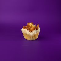A bacon butter pecan cupcake topped with maple buttercream and finished with a waffle piece, bacon pieces, and maple syrup. Bacon & Waffles cupcake
