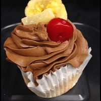 A banana cupcake filled with strawberry cream cheese, topped with chocolate buttercream and finished with a cherry, a banana chip and a dried pineapple tidbit. Banana Split cupcake