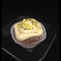 A lemon cupcake topped with honey cream cheese icing and finished with yellow and black nonpareils. Honey Lemon cupcake