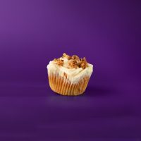A cupcake with a light white cake base with roasted coconut and pecans, topped with cream cheese icing and chopped pecans, a Granny B original. Italian Cream cupcake