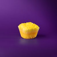 A lemon cupcake with lemon buttercream topped with crushed lemon heads. Lemon cupcake