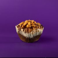 A brownie-cake cupcake filled with peanut butter and chocolate chips, topped with peanut butter buttercream, and finished with a chocolate ganache drizzle and peanut butter chips. Buckeye cupcake