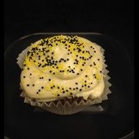 A honey cupcake topped with honey cream cheese and finished with black and yellow nonpareils. Honey cupcake