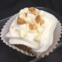 A white chocolate cupcake with chopped macadamia nuts baked in, topped with a vanilla buttercream and finished with white morsels and finely chopped macadamia nuts. White Chocolate Macadamia Nut cupcake