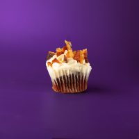 A red velvet cupcake with a crumbled bacon and maple syrup mixture filling, topped with cream cheese icing, bacon pieces and a maple syrup drizzle. Christmas Morning cupcake