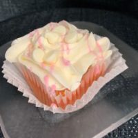A strawberry cupcake with a white ganache filling, cream cheese icing, strawberry ganache drizzle, and topped with white morsels. White Chocolate Strawberry cupcake