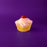 A vanilla cupcake with a cherry ganache filling, cherry cream cheese icing, white ganache drizzle, and a cherry on top. White Chocolate Cherry